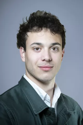 Un jeune homme aux yeux marrons clairs sourit à l'écran