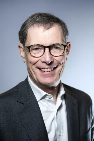 Un homme brun portant des lunettes sourit à l'objectif