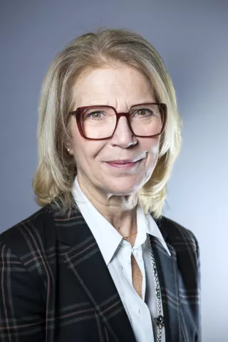 Une femme blonde aux lunettes bordeaux sourit à l'écran