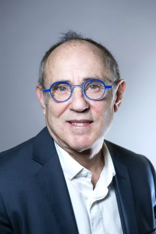 Un homme portant des lunettes bleu sourit à l'écran